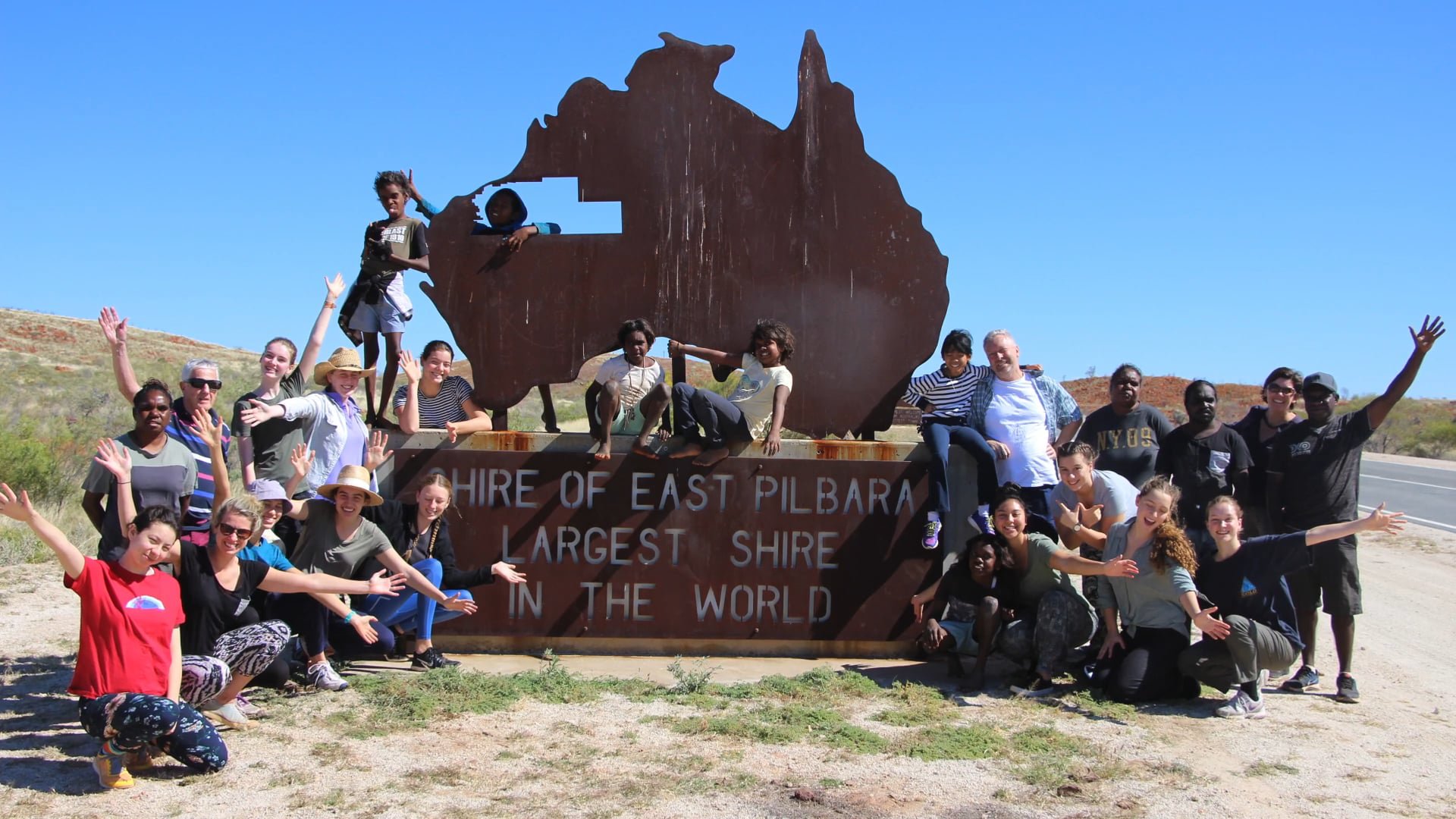 Group Waving to the Camera by the Large East Pilbara Shire Signage