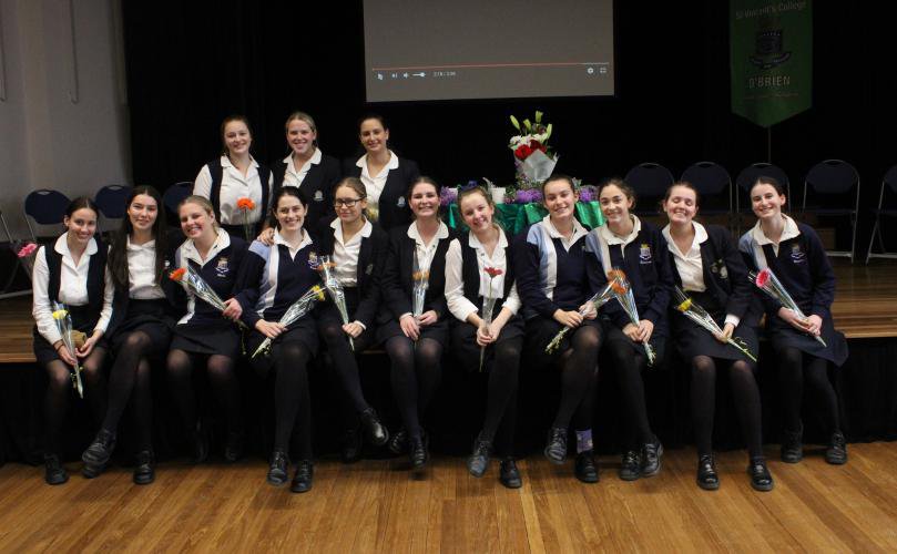 Students Posed in Front of the Stage in Winter Uniform Holding a Flower Each